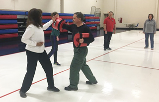 Saluqi Success Pathway Coach Brenda Rayner learns the block and parry technique from Officer Joe Benya during the second night of R.A.D. certification training inside the Nabors Gymnasium.