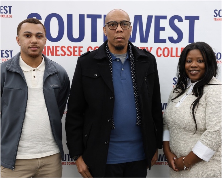 Three individuals stand smiling before a Southwest Tennessee Community College backdrop, dressed in professional attire, posing for a campus event photo.