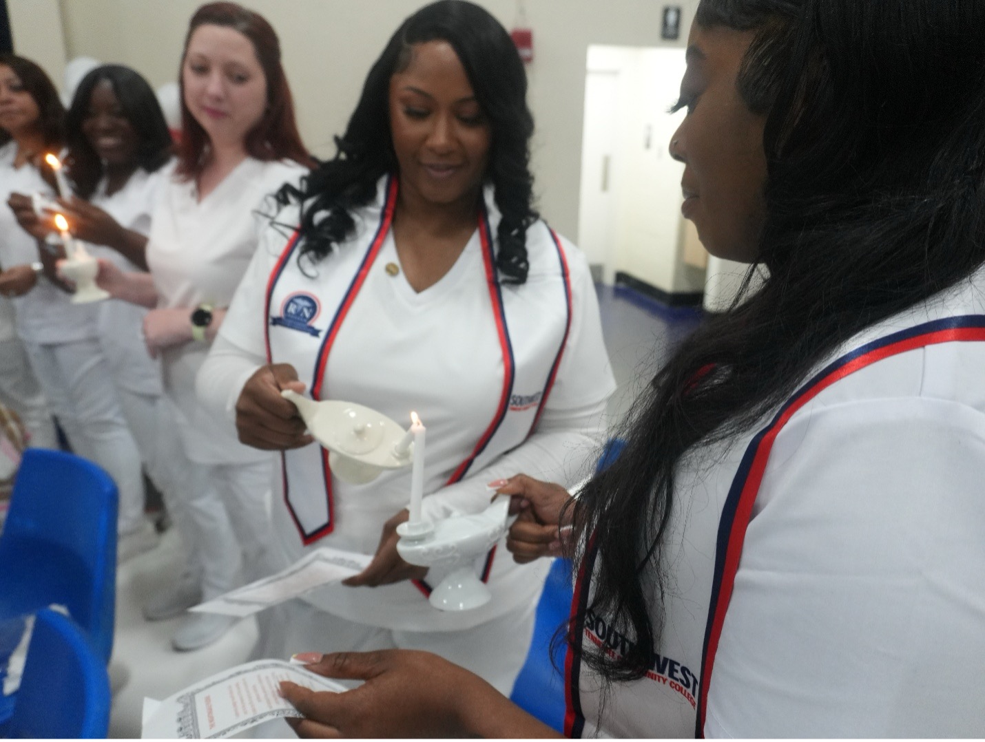 Nursing students in white uniforms participate in a candlelight ceremony. Each person lights a candle from another, symbolizing tradition and unity. “RN” and “Southwest Tennessee Community College” are visible on uniforms.
