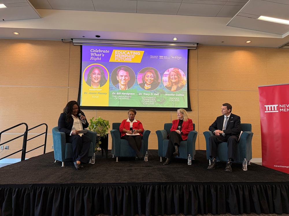 A panel discussion is taking place on a stage with four individuals seated in upholstered chairs arranged in a row. A person on the far left holds a microphone as they speak. The other three panelists are seated with notebooks or papers in hand. Behind them, a large screen displays event graphics with text and circular photos. To the right of the stage, a tall red banner with the New Memphis logo is visible. The room has warm-colored walls, ceiling lights, and an elevated platform with black skirting.
