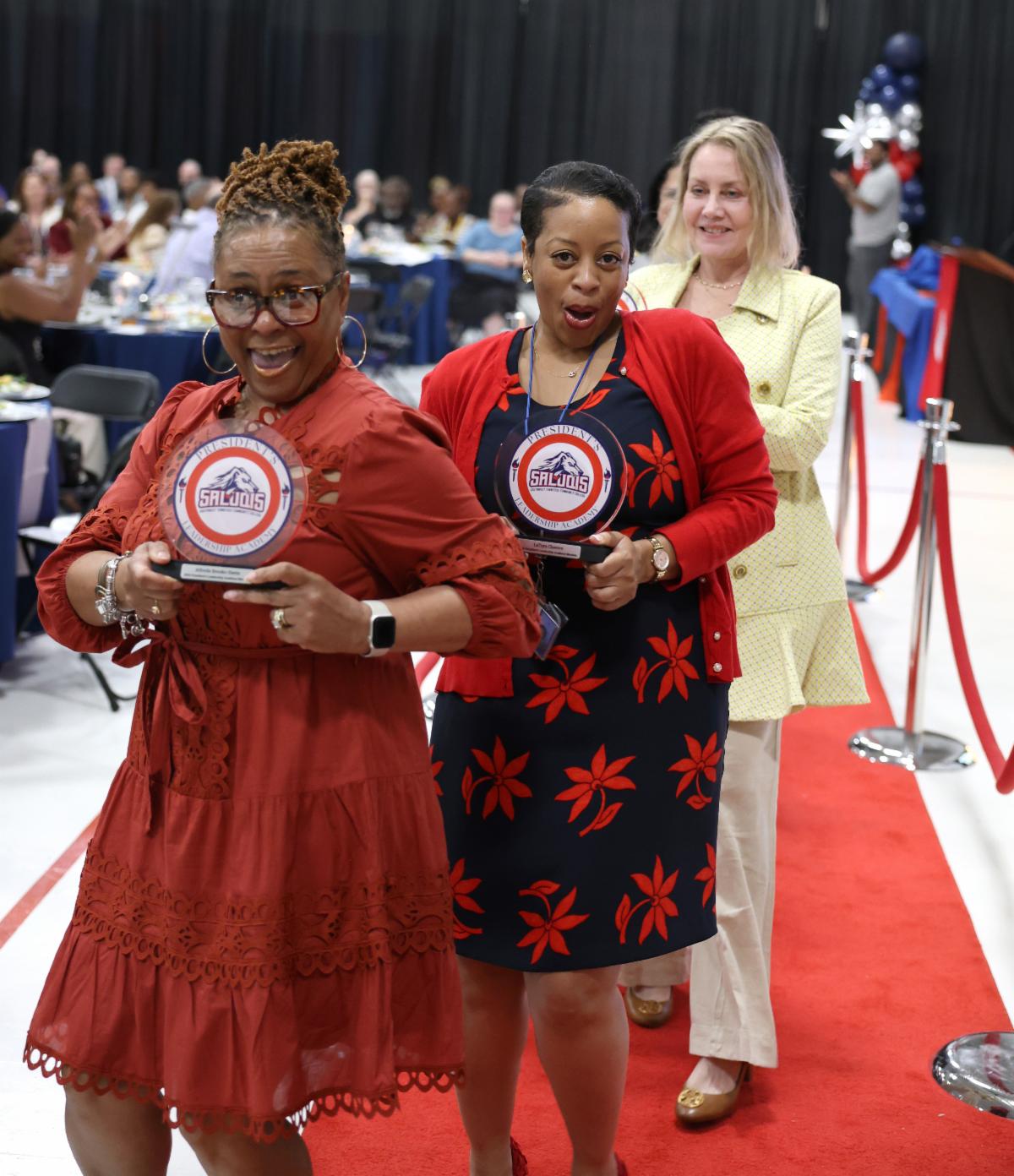 3 women walking down a red carpet holding their awards